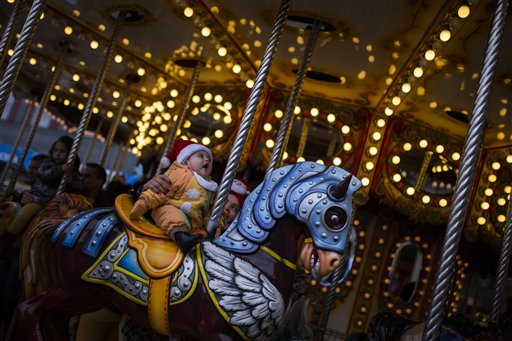 A woman holds her baby as they ride on a carrousel at Madrid's Christmas market in Madrid, Spain, Saturday, Dec. 13, 2014. AP