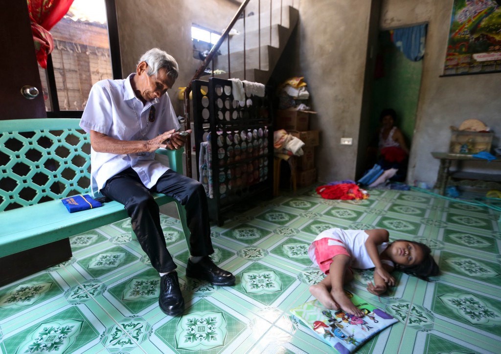 World War II veteran Porferio G. Laguitan, 91 years old, checking his mobilephone while one of his grandchildren plays on the floor insid ehis home in Taguig City. INQUIRER PHOTO/LYN RILLON
