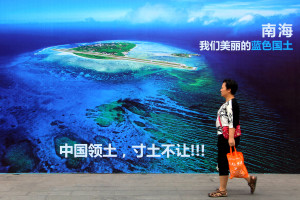 FILE - In this July 14, 2016 file photo, a woman walks past a billboard featuring an image of an island in South China Sea on display with Chinese words that read: "South China Sea, our beautiful motherland, we won't let go an inch" in Weifang in east China's Shandong province. An international arbitration panel’s decision on the contested waters of the South China Sea so far is fueling regional tensions rather than tamping them down. In the ensuing 11 days, China has responded to the sweeping victory for the Philippines by flexing its military might. The Philippines faces pressure both at home and abroad not to cede an inch to China after the July 12 decision by a tribunal at The Hague-based Permanent Court of Arbitration. (Chinatopix via AP, File)