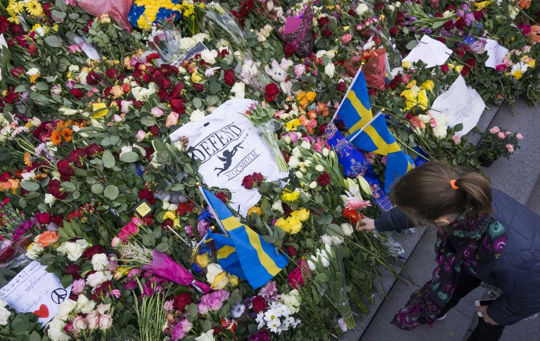 A girl lays a flower on April 9, 2017 at a makeshift memorial near the point where a truck drove into a department store in Stockholm, Sweden. Four people died and fifteen were injured when a truck plunged into a crowd at a busy pedestrian street in the Swedish capital on April 7, 2017. / AFP PHOTO / Jonathan NACKSTRAND