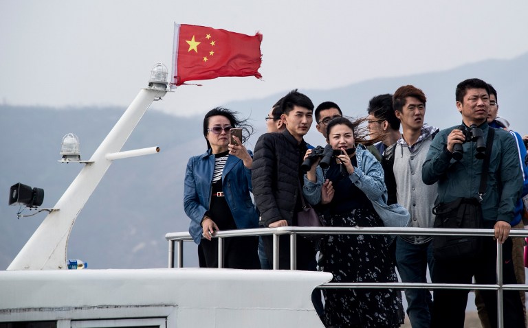 Chinese tourists try to catch a glimpse of North Korean soldiers from a boat on the Yalu river near Sinuiju, opposite the Chinese border city of Dandong, on April 16, 2017. Dandong city is the main crossing point to North Korea, and every day hundreds of tourists embark on small boats for a cruise on the Yalu border river and a fleeting glimpse of another world. / AFP PHOTO / Johannes EISELE