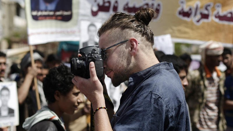 In this Tuesday, April 16, 2013 photo, Luke Somers, 33, an American photojournalist who was kidnapped over a year ago by al-Qaida, uses a camera during a demonstration demanding the release of Yemeni detainees in Guantanamo Bay prison in front of the U.S. embassy in Sanaa, Yemen. Somers and a South African teacher held by al-Qaida militants in Yemen were killed Saturday, Dec. 6, 2014 during a U.S.-led rescue attempt, a raid President Barack Obama said he ordered over an "imminent danger" to the reporter. (AP Photo/Hani Mohammed)