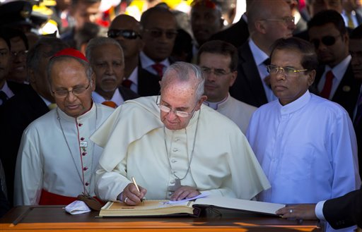 Pope Francis writes in a book with Sri Lankan President Maithripala Sirisena, right, standing beside him at the airport in Colombo, Sri Lanka, Tuesday, Jan. 13, 2015.  AP
