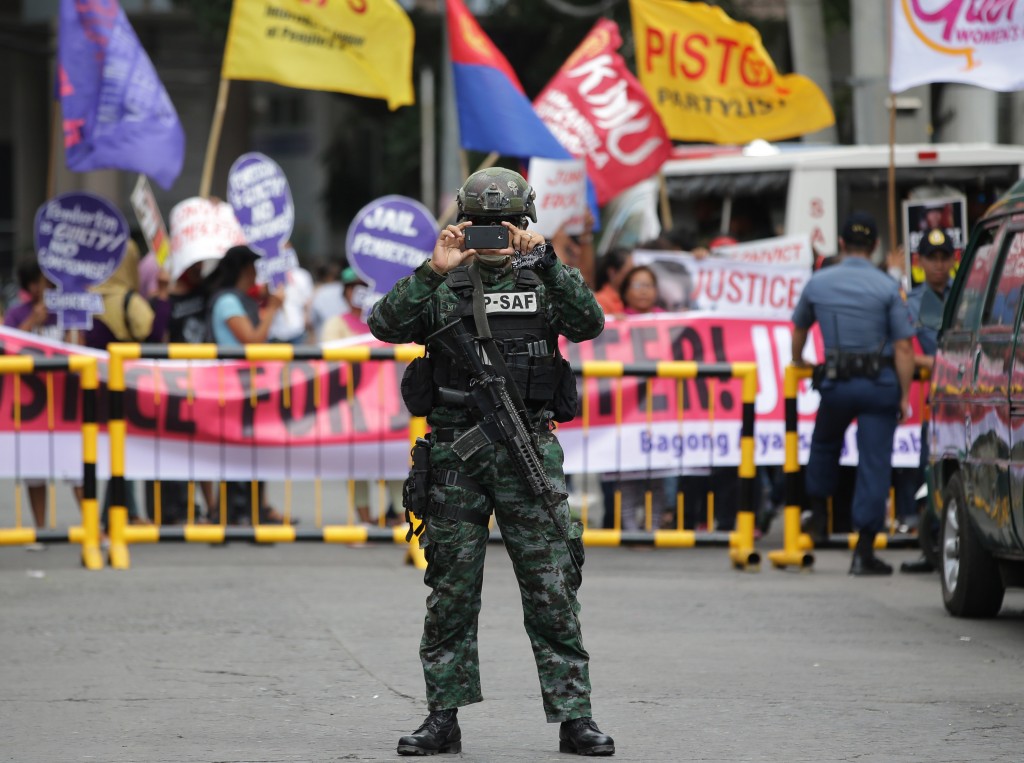 A Philippine Special Action Force police takes a photo beside protesters outside the courts at Olongapo city, Zambales province, northwest of Manila, Philippines Tuesday Dec. 1, 2015. AP 