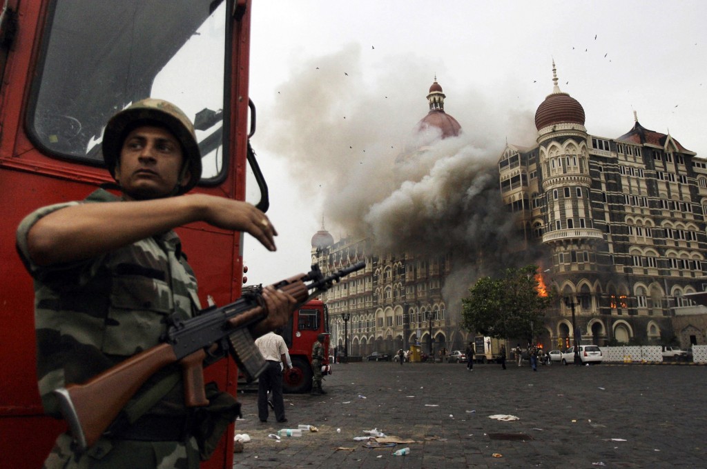 FILE- In this Nov. 29, 2008, file photo, an Indian soldier takes cover as the Taj Mahal hotel burns during gun battle between Indian military and militants inside the hotel in Mumbai, India. A Pakistani-American who helped plan a 2008 attack on India's financial hub has told a court in India that he traveled to India seven times to scout potential targets for a Pakistan-based group. (AP Photo/David Guttenfelder, File)