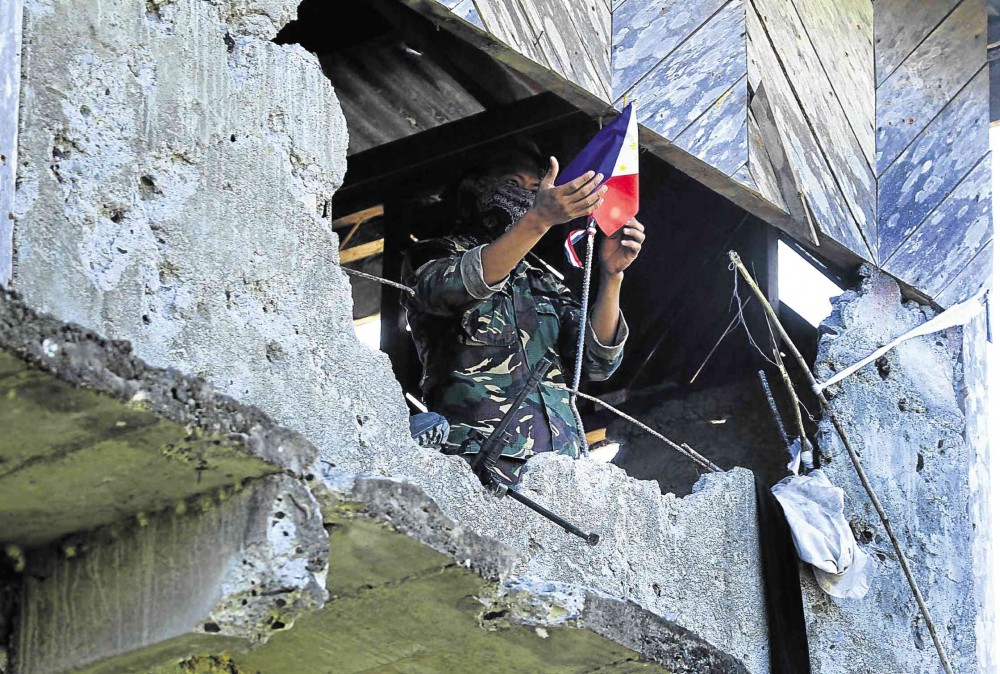 AFTERMATH OF TERRORIST ATTACK A week after gunmen waving black flags of the Islamic State (IS) group attacked a military outpost, a soldier stands before a Philippine flaglet tied to an exposed iron bar of a bullet-riddled house in Butig town, Lanao del Sur province. AFP