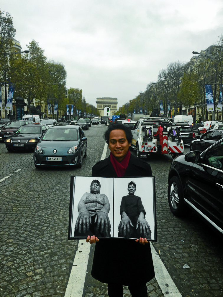 RYAN ARBILOholds two of his photographs in themiddle of Avenue des Champs-Élysées NIKKODIZON