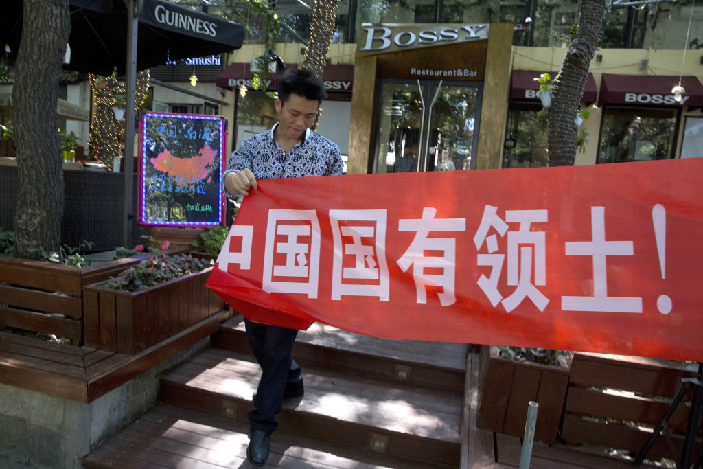 A worker of a restaurant bar puts up a banner which partly reads: "South China Sea is China's territory" in Beijing Wednesday, July 13, 2016. China warned other countries Wednesday against threatening its security in the South China Sea after an international tribunal handed the Philippines a victory by saying Beijing had no legal basis for its expansive claims there. (AP Photo/Ng Han Guan)