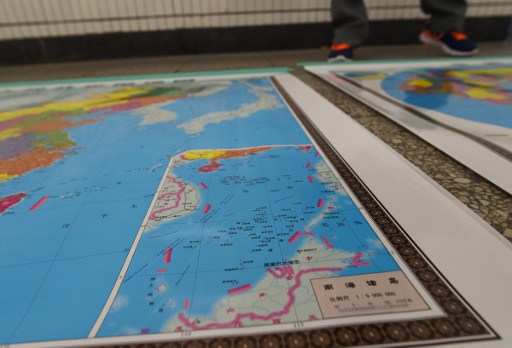In this photo taken on June 15, 2016 a vendor stands behind a map of China including an insert with red dotted lines showing China's claimed territory in the South China Sea, in Beijing.  Chinese pressure was blamed June 16 for a stunning diplomatic U-turn by Southeast Asian Nations that saw them retract a statement sounding alarm over Beijing's island building in the South China Sea. China claims nearly all of the South China Sea -- a vast tract of water through which a huge chunk of global shipping passes. The Philippines, Taiwan, Brunei, Malaysia and Vietnam have competing claims to parts of the sea, which is believed to harbour significant oil and gas deposits. / AFP PHOTO / GREG BAKER