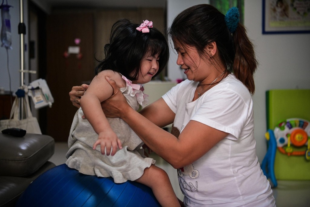 Josefina Amparo Hosena (right) carries Leona Heng, who suffers from Edwards syndrome, onto an exercise ball as part of her therapy. ST PHOTO: MARK CHEONG