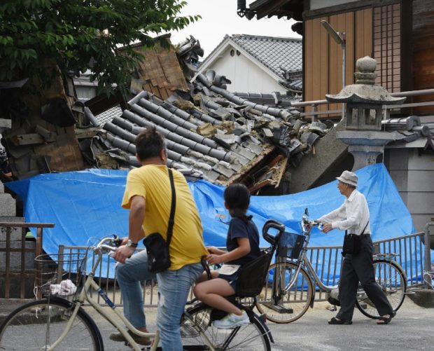 People pause to look at a collapsed house following an earthquake quake in Ibaraki City, north of Osaka prefecture on June 18, 2018.  At least two people, including a child, were killed on June 18, after a strong quake rocked the second city of Osaka during the morning rush hour, Japan's government said. / AFP PHOTO / JIJI PRESS / STR / Japan OUT