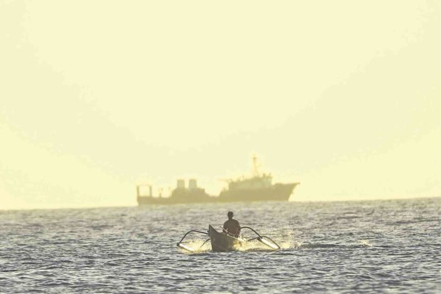 A Filipino fisherman in a banca moves away from a Chinese Coast Guard vessel at Panatag (Scarborough) Shoal in the West Philippine Sea.