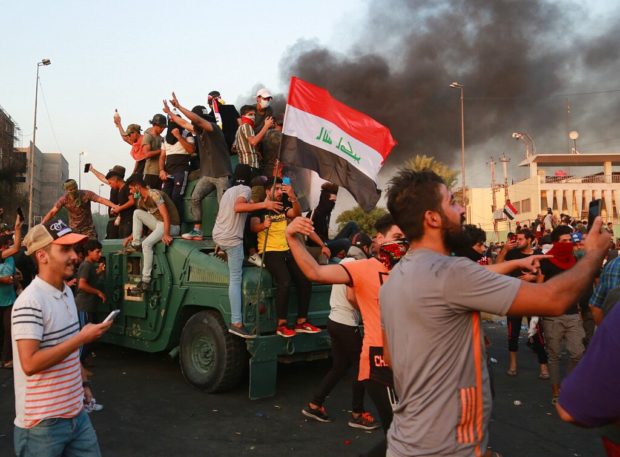 Anti-government protesters take over an armored vehicle before they burn it during a demonstration in Baghdad, Iraq, Thursday, Oct. 3, 2019. Iraqi security forces fired live bullets into the air and used tear gas against a few hundred protesters in central Baghdad on Thursday, hours after a curfew was announced in the Iraqi capital on the heels of two days of deadly violence that gripped the country amid anti-government protests. (AP Photo/Hadi Mizban)
