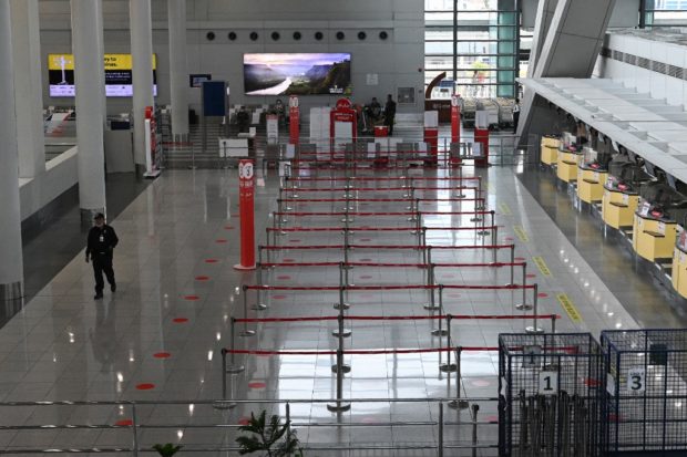 A security officer (L) walks past empty check-in counters at the airport in Manila on August 4, 2020, after all domestic flights were cancelled following new restrictions to combat the COVID-19 coronavirus outbreak. - More than 27 million people -- a quarter of the Philippine population -- were give 24-hours notice of the new restrictions that have shuttered many businesses, halted public transport and grounded flights in the capital and four surrounding provinces as the government battles to rein in the virus. (Photo by Ted ALJIBE / AFP)