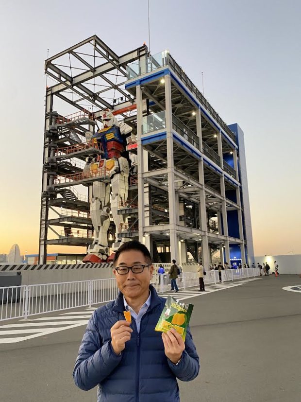 Japanese Ambassador to the Philippines Koshikawa Kazuhiko at the Gundam statue in Yokohama, Japan while holding dried mangoes from the Philippines.