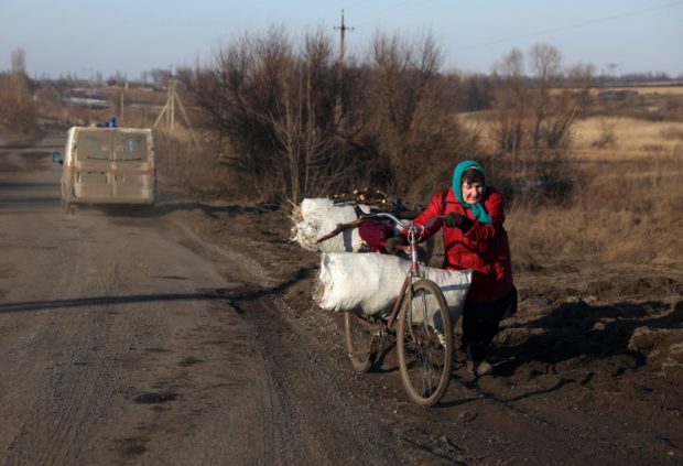 An elderly woman pushes her bicycle loaded with hay and brushwood on a roadside near village of Kolisnykivka, in the Kharkiv region on February 23, 2023, amid the Russian invasion of Ukraine. (Photo by Anatolii Stepanov / AFP)