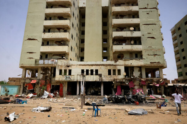 A man walks past near a damaged car and buildings at the central market in Khartoum North