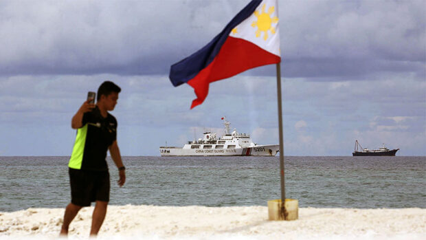 PH TERRITORY A Philippine Navy sailor displays the country’s flag on Sandy Cay, a sandbar just 7.4 kilometers (4 nautical miles) from Pag-asa Island in the West Philippine Sea, in this June 2022 photo. Chinese naval ships have been patrolling the area.—MARIANNE BERMUDEZ china harassment fishers senate reso