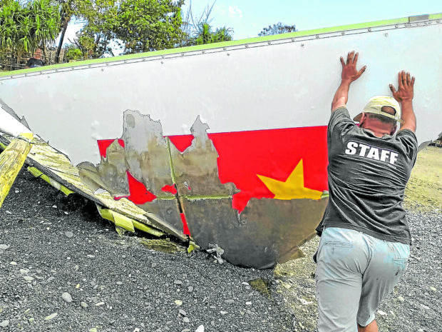 A local resident pushes upright a metal debris, which fell from the sky in Calintaan, Occidental Mindoro, in 2022. The fallen metal shows a part of a yellow star inside a red rectangle of what looks like a flag.