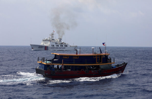 FILE PHOTO: A Philippine supply boat sails near a Chinese Coast Guard ship during a resupply mission for Filipino troops stationed at a grounded warship in the South China Sea, October 4, 2023. 
