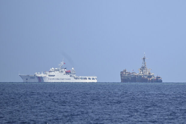This photo taken on August 22, 2023 shows a Chinese coast guard ship (L) sailing past the grounded Philippine navy ship BRP Sierra Madre where marines are stationed to assert Manila's territorial claims in the disputed South China Sea. A team of AFP journalists on board the BRP Cabra, one of the two Philippine Coast Guard escort boats, watched as one of the Chinese ships came within several meters of the vessel. AFP was one of three media outlets given the rare opportunity to join the Philippine resupply mission to Second Thomas Shoal, less than three weeks after Chinese coast guard ships water cannoned a similar replenishment operation. (Photo by Ted ALJIBE / AFP)