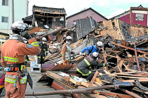 Firefighters search for people in therubble of a collapsed house in the city of Wajima, Ishikawa prefecture, which was hit by a quake on New Year’s Day. Over 50 people have been reported missing. 