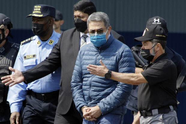 Former Honduran President Juan Orlando Hernandez, second from right, is taken in handcuffs to a waiting aircraft