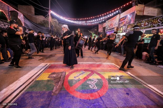 Shiite Muslim devotees self-flagellate over an unfurled banner on the ground depicting the Pride rainbow flag defaced with a boot and the Arabic slogan "no to homosexual society" as they participate in a mourning procession during the ten-day period at the start of the Muslim month of Muharram ahead of Ashura, in remembrance of the seventh century killing of Prophet Mohammed's grandson Imam Hussein, in the city of Nasiriyah in Iraq's southern Dhi Qar province on July 25, 2023. (Photo by Asaad NIAZI / AFP)