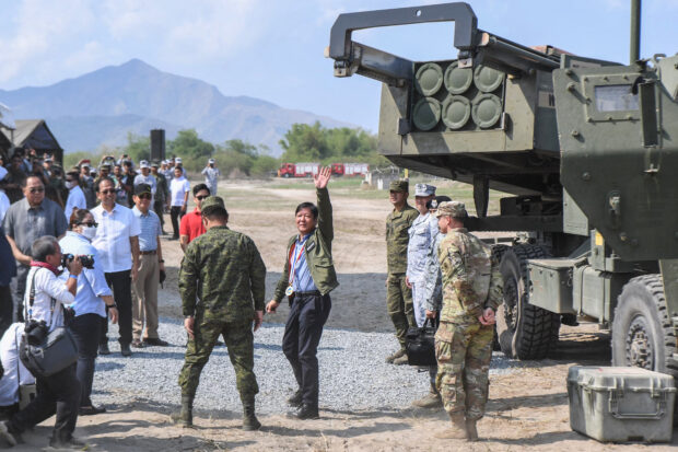 This file photo taken on April 26, 2023 shows Philippine President Ferdinand Marcos (C) waving to photographers after inspecting a high mobility artillery rocket system (HIMARS) before a live fire exercise as part of the US-Philippines Balikatan joint exercise at the naval training base in San Antonio, Zambales province. 