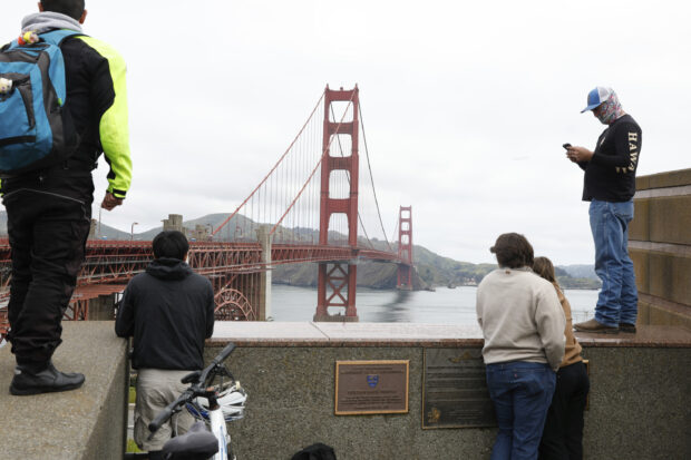 Pedestrians and bicyclists wait outside the pedestrian gate on the south side of the Golden Gate Bridge while the bridge is closed due to protesters on Monday, April 15, 2024 in San Francisco, California