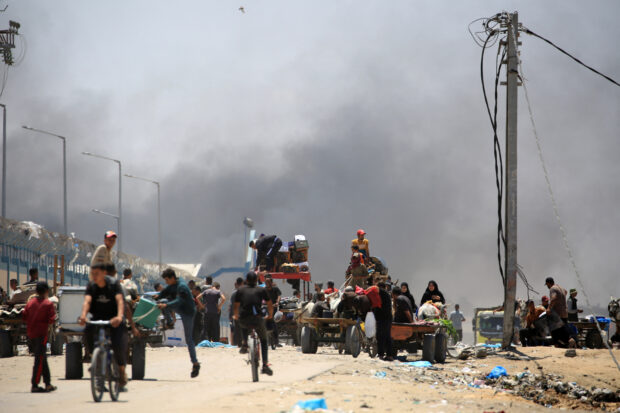 Palestinians flee with their belongings as smoke rises in the background, in the area of Tel al-Sultan in Rafah in the southern Gaza Strip on May 30, 2024, amid the ongoing conflict between Israel and the militant group Hamas