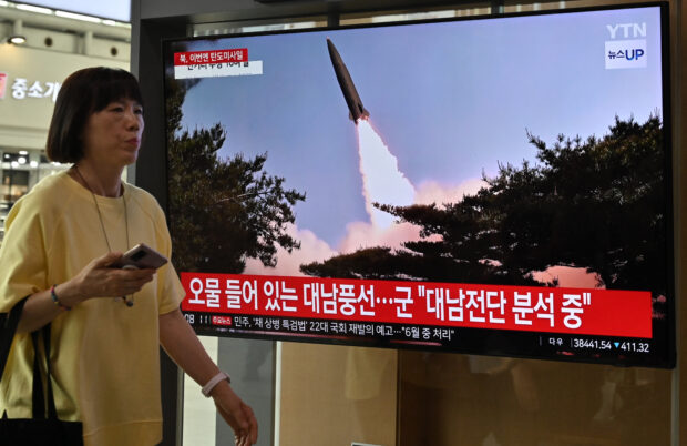 A woman walks past a television screen showing a news broadcast with file footage of a North Korean missile test, at a train station in Seoul on May 30, 2024. North Korea fired a salvo of short-range ballistic missiles early May 30, Seoul's military said, hours after Pyongyang sent hundreds of trash-filled balloons across the border to punish South Korea.