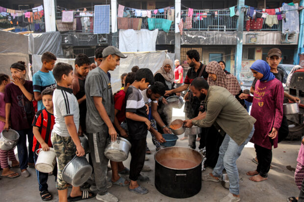 Children queue with pots to receive food aid from a kitchen at the Abu Zeitun school run by the UN Relief and Works Agency for Palestine Refugees (UNRWA) in the Jabalia camp for Palestinian refugees in the northern Gaza Strip on June 13, 2024 amid the ongoing conflict