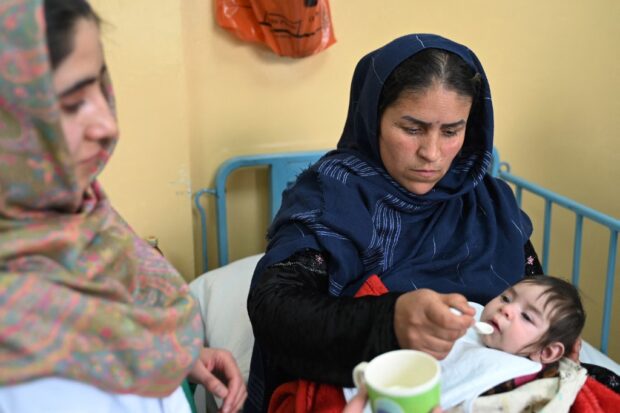 This photograph taken on February 26, 2024 shows Samira (L), an Afghan nurse, holding a cup of milk for a patient in the malnutrition ward of the government hospital in Baharak district of Badakhshan province. 