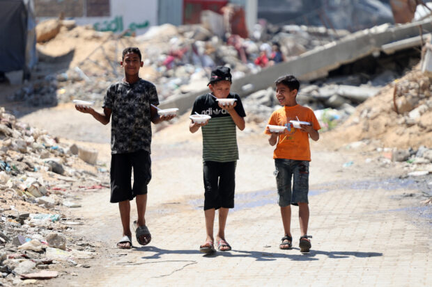 Three Palestinian boys carry two bowls of food each, as the make their way along a street past the rubble of buildings destroyed in previous Israeli bombardment, in the Sheikh Radwan neighbourhood, north of Gaza City on July 3, 2024, amid the ongoing conflict between Israel and the militant Hamas group. Israel's military said on July 3, it was conducting raids backed by air strikes in northern Gaza, killing "dozens" of militants in an area where it had declared the command structure of Hamas dismantled months ago. 