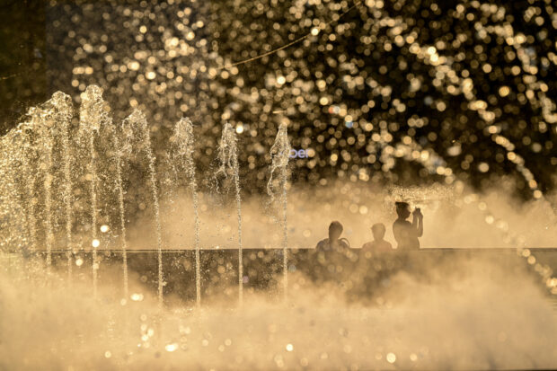 People are pictured in the mist of a fountain in downtown Bucharest on July 17, 2024, as Romania experiences a heatwave with temperatures reaching 42 degrees Celsius in the southern regions of the country.