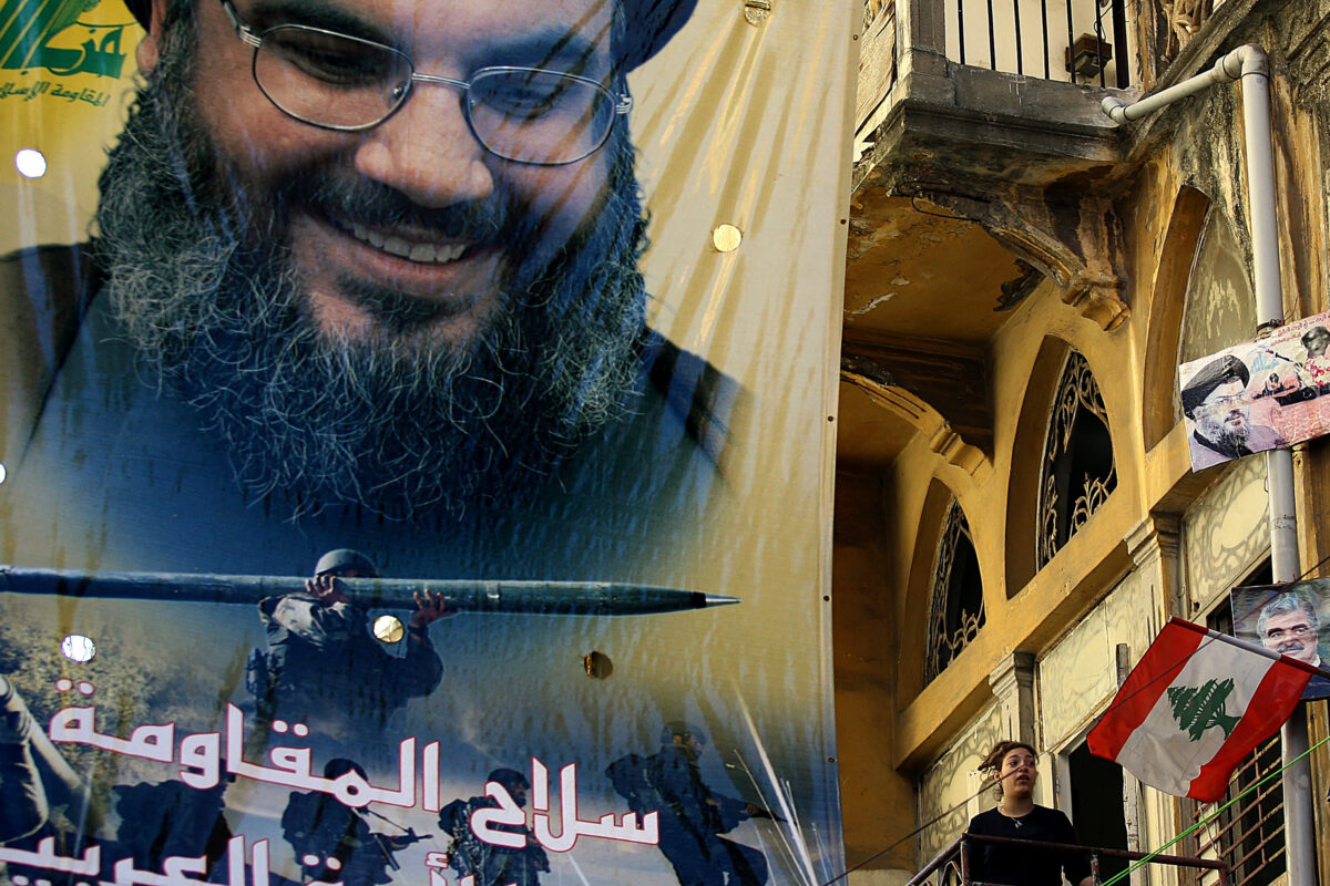 A large poster of Hezbollah chief Hassan Nasrallah bearing the slogan "The weapons of the resistance is the pride of the Arab Nations," hangs above a woman standing on her balcony in a Beirut street, on November 20, 2006. - Lebanon's Iran-backed Hezbollah group confirmed on September 28, 2024 that its leader Hassan Nasrallah had been killed, after Israel said it had "eliminated" him in a strike on south Beirut a day earlier.