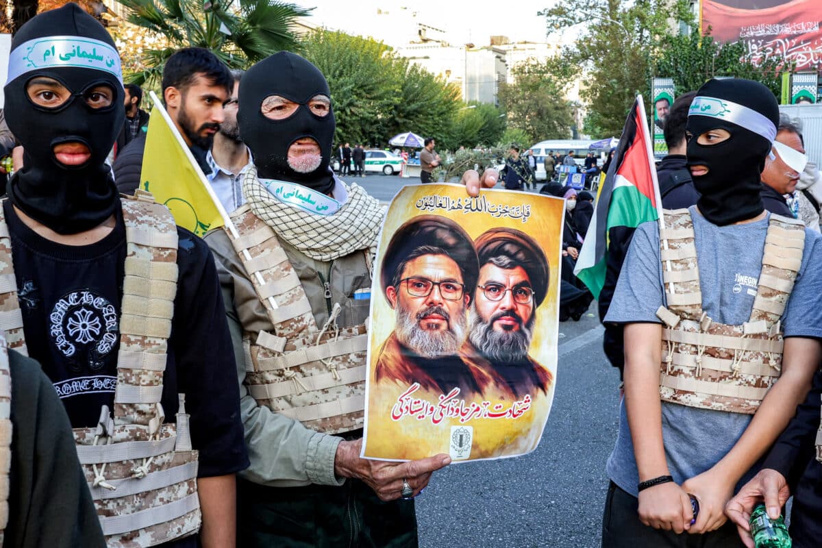 Masked demonstrators stand next to one holding a poster depicting the faces of Lebanese Hezbollah's slain leader Hassan Nasrallah and Executive Council chief Hashem Safieddine, during an anti-Israel rally in Tehran on October 24, 2024.