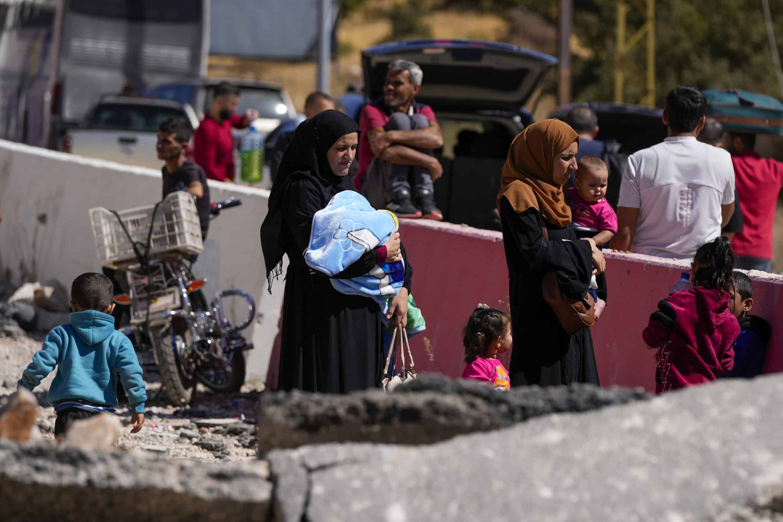 People carry their luggage as they cross into Syria on foot, through a crater caused by Israeli airstrikes aiming to block Beirut-Damascus highway at the Masnaa crossing, in the eastern Bekaa Valley, Lebanon, Saturday, Oct. 5, 2024. (AP Photo/Hassan Ammar)