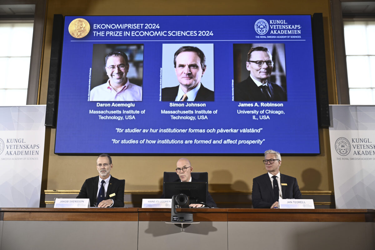 Academy of Sciences permanent secretary Hans Ellegren, center, Jakob Svensson, left, and Jan Teorell, of the Nobel assembly announce the Nobel memorial prize in economics winners, Daron Acemoglu, Simon Johnson and James A Robinson, seen on screen, during a press meeting at the Royal Swedish Academy of Sciences in Stockholm, Sweden, Monday Oct. 14, 2024. (Christine Ol