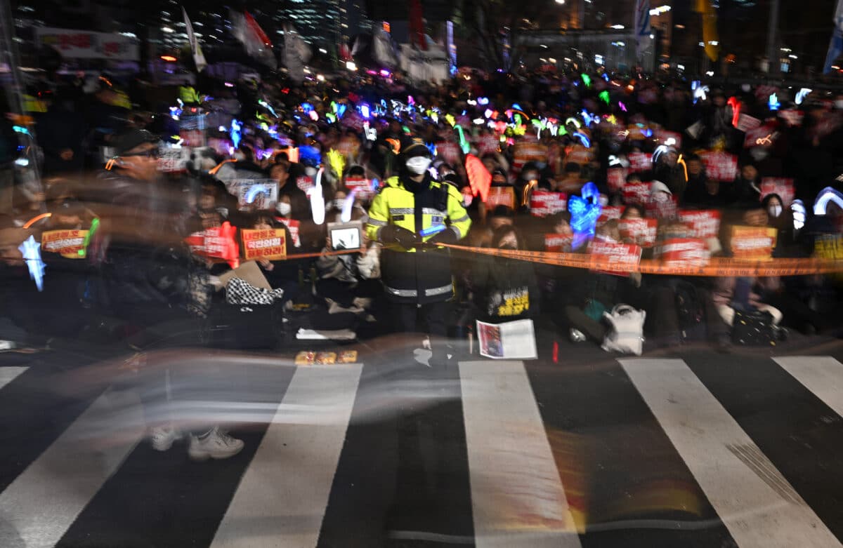 A police officer holds a line on a crosswalk as protesters take part in a demonstration demanding President Yoon Suk Yeol's resignation outside the National Assembly in Seoul on December 10, 2024. - South Korean authorities banned more top officials from leaving the country on December 10, in the wake of President Yoon Suk Yeol's bungled attempt to impose martial law.