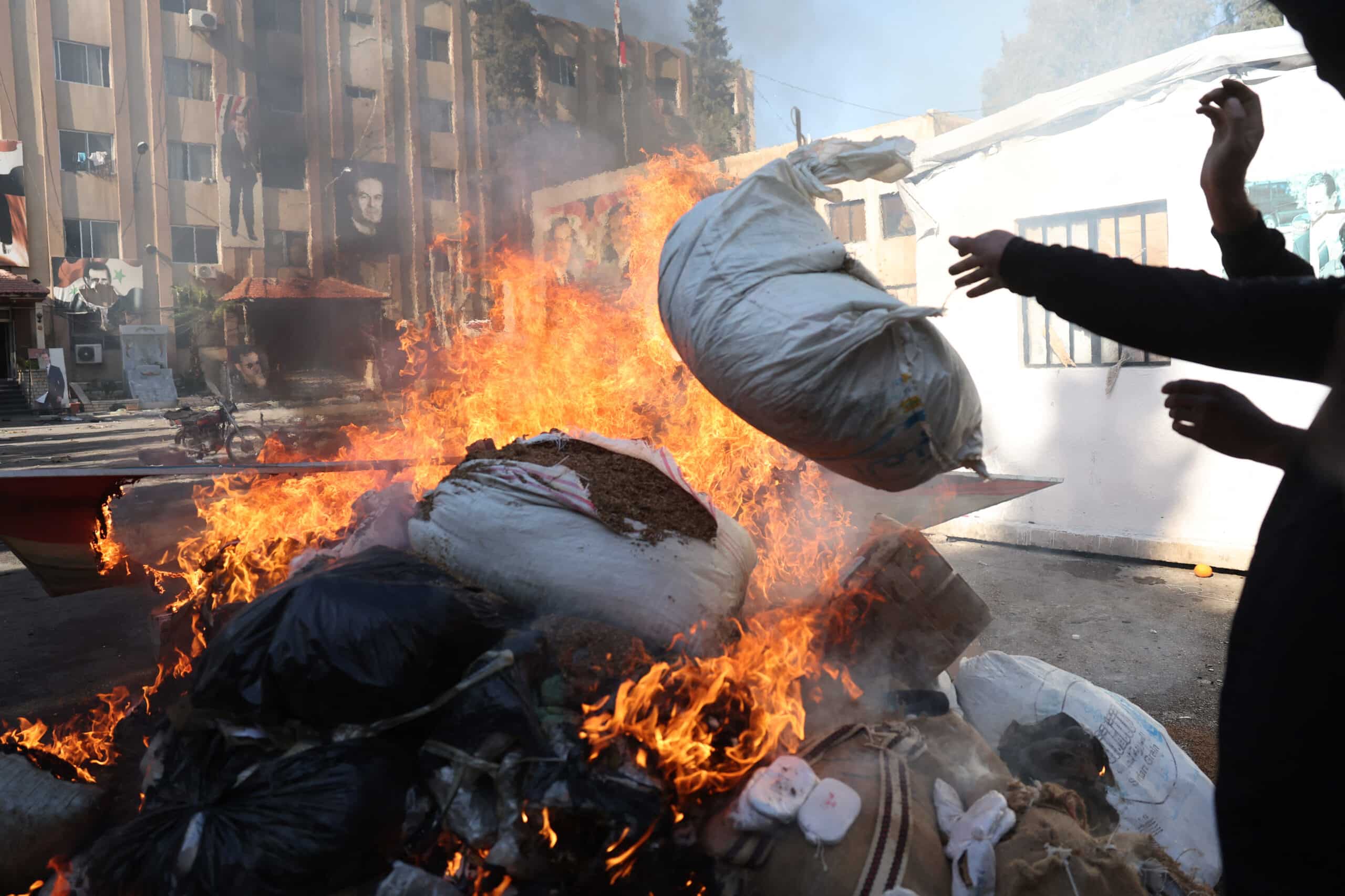 A man throws a bag onto a pile of burning illicit drugs, as Syria's new authorities burn drugs reportedly seized from a security branch, in Damascus on December 25, 2024. - Syria's new authorities torched a large stockpile of drugs on Wednesday, two security officials told AFP, including one million pills of captagon, whose industrial-scale production flourished under ousted president Bashar al-Assad. (Photo by OMAR HAJ KADOUR / AFP)